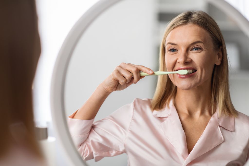 beautiful-mature-female-brushing-her-teeth-with-toothbrush-near-mirror-home.jpg